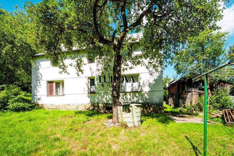 Ein Einfamilienhaus in Lúky mit einem großen Baum, einer Rasenfläche und einem Holzschuppen.