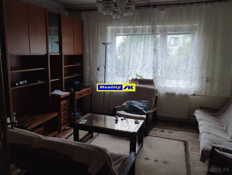 Wohnzimmer in einem Einfamilienhaus mit Holzmöbeln, Couchtisch und Vorhängen.