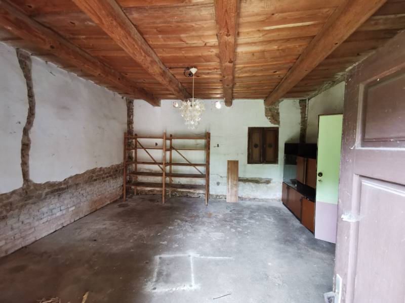 Innenraum eines Einfamilienhauses mit Holzbalkendecke, einfachem Regal und Schrank.