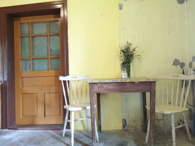 Gelbe Wände in einem Einfamilienhaus mit einem Holztisch, Stühlen und einer kleinen Vase mit Blumen.
