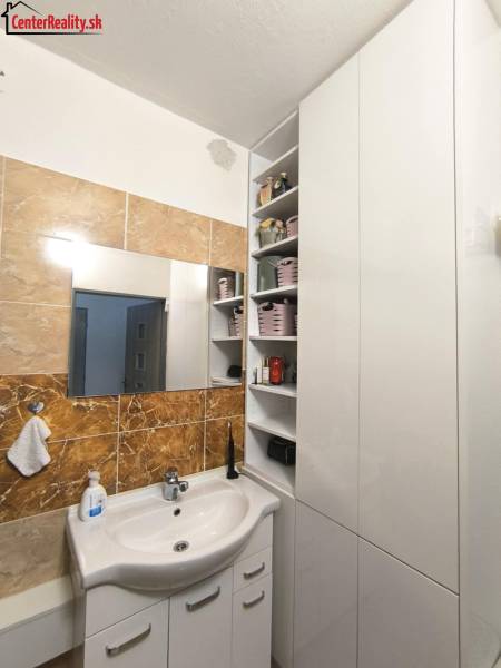 Badezimmer in einer 3-Zimmer-Wohnung mit weißem Waschbecken, Spiegel und Aufbewahrungsschränken.