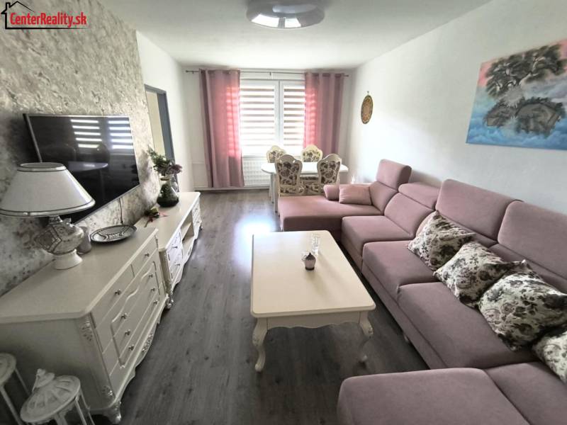 Wohnzimmer in einer 3-Zimmer-Wohnung mit rosa Sofa, Tisch und Dekorationen auf der Kommode.