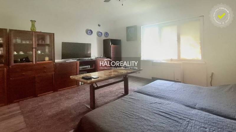 Wohnzimmer eines Einfamilienhauses mit älteren Möbeln, Fernseher und dekorativen Tellern an der Wand.