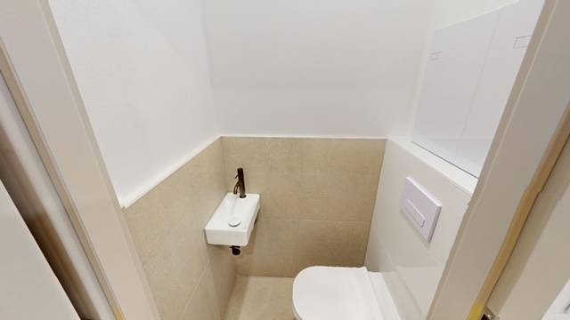 Kompakte Toilette mit Waschbecken in einer 2-Zimmer-Wohnung, beigefarbene Fliesen und weiße Wand.