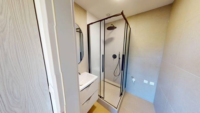 Badezimmer in einer 2-Zimmer-Wohnung mit Duschkabine und Waschbecken.