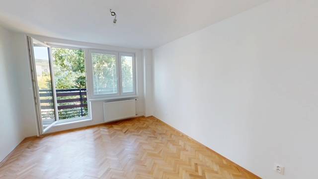 Ein geräumiges Zimmer in einer 2-Zimmer-Wohnung mit Holzboden und einem großen Fenster zum Balkon.