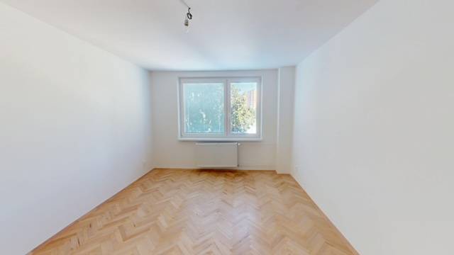 Ein Zimmer mit Parkettboden in einer hellen 2-Zimmer-Wohnung, ein Fenster mit Blick auf Bäume.