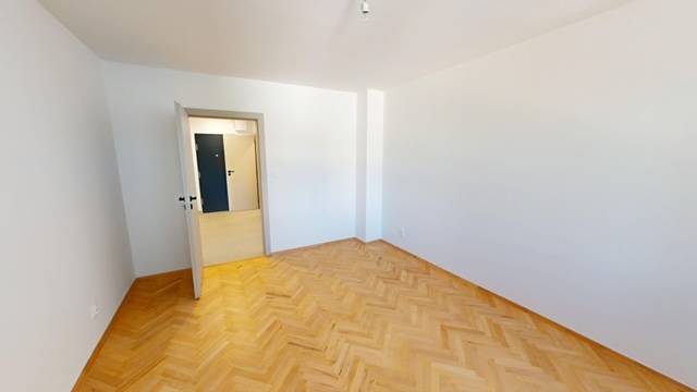 Ein Zimmer in einer 2-Zimmer-Wohnung mit Parkettboden und weißen Wänden.