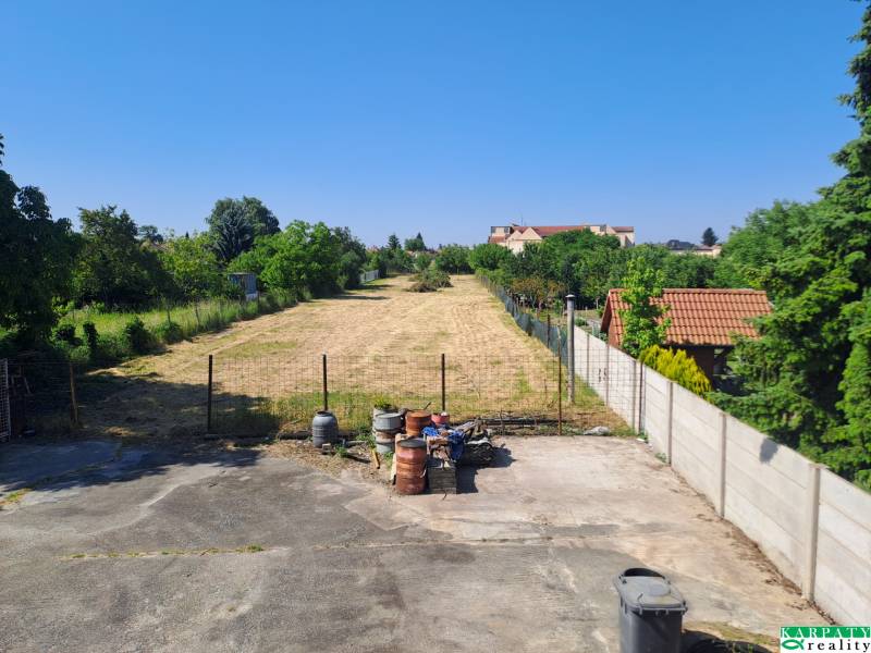 Befestigte Fläche mit Grünflächen, Fässern und Häusern in Sládkovičovo, Einfamilienhäuser im Hintergrund.