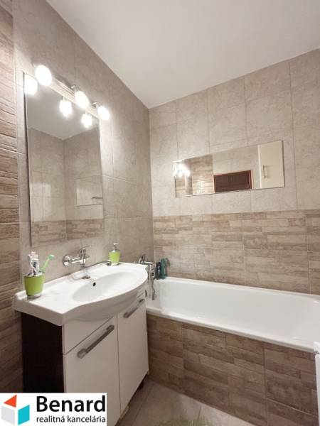 Badezimmer in einer 2-Zimmer-Wohnung mit Badewanne und Waschbecken, helle Fliesen, Spiegel.