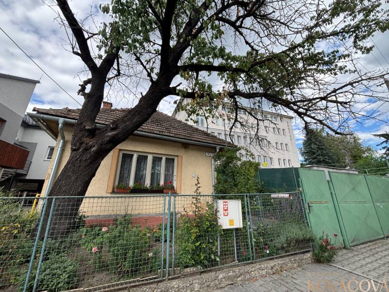 Ein Einfamilienhaus in Ilava mit einem eingezäunten Garten, einem Baum und angrenzenden Gebäuden im Hintergrund.