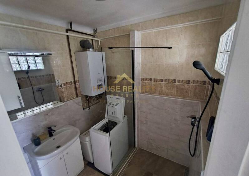 Badezimmer in einer 2-Zimmer-Wohnung mit Dusche, Waschmaschine, Waschbecken und Boiler.