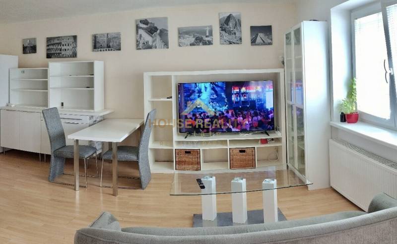 Wohnzimmer in einer Zweizimmerwohnung mit Fernseher, Sofa und Esstisch.