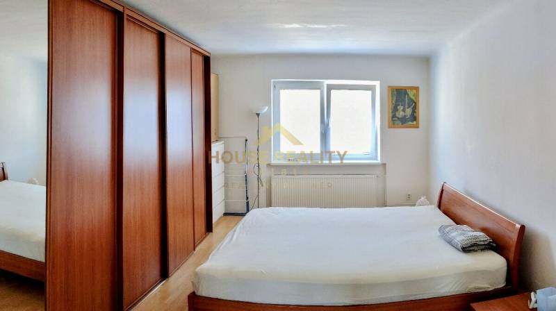 Schlafzimmer mit einem Holzbett und einem Schrank in einer 2-Zimmer-Wohnung, ergänzt durch ein Fenster und ein Bild.