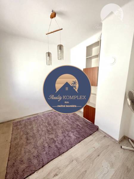Ein Zimmer in einem Einfamilienhaus mit einem lila Teppich, einer Holzleuchte und einem eingebauten Regal.