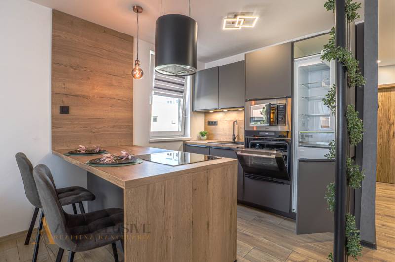 Küche in einer 3-Zimmer-Wohnung mit Holztheke, Geräten und moderner Beleuchtung.