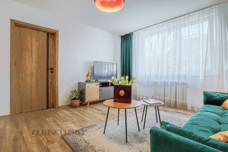 Wohnzimmer in einer 3-Zimmer-Wohnung mit Sofa, Fernseher und Tisch mit Blumen.