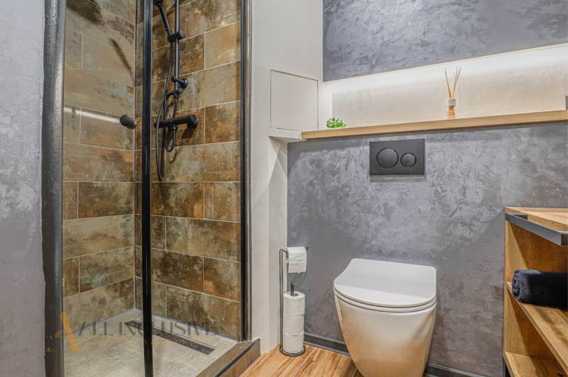 Badezimmer mit Toilette und Dusche in einer 3-Zimmer-Wohnung, mit grauen Wänden und Holzakzenten.