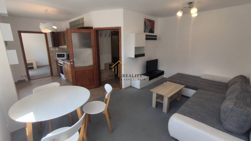 Wohnzimmer einer Zweizimmerwohnung mit Sitzgarnitur, Esstisch und Kochnische.