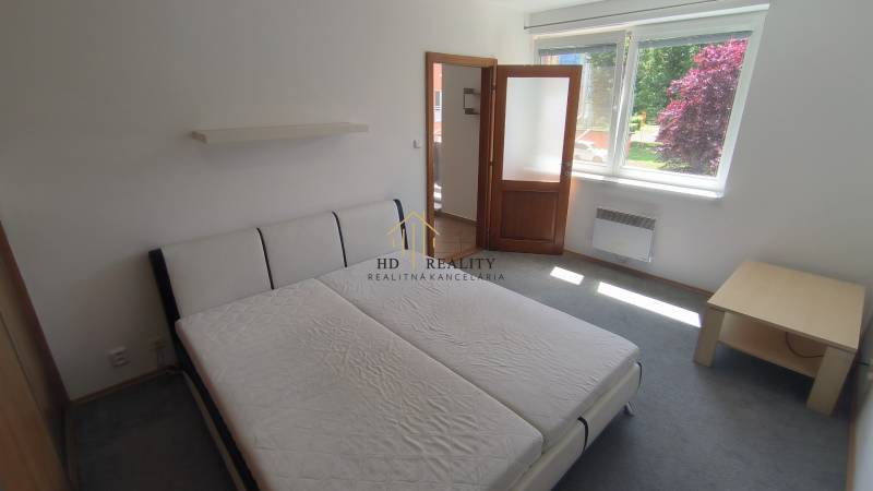Helles Zimmer mit Bett, Nachttisch und Fenster, geeignet für eine 2-Zimmer-Wohnung.