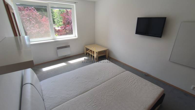 Schlafzimmer in einer 2-Zimmer-Wohnung mit Fernseher, Bett und Blick in den Garten.
