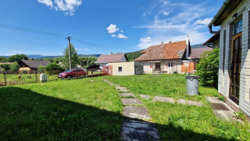 Ein Einfamilienhaus in Mníšek nad Hnilcom mit Rasen, Terrasse und Parkplatz unter klarem Himmel.