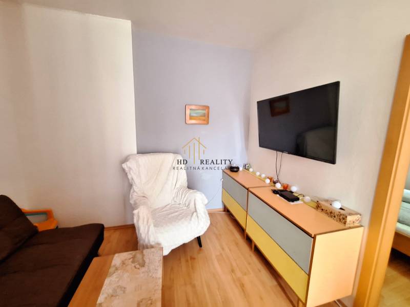 Wohnzimmer in einer 3-Zimmer-Wohnung, mit einem Fernseher an der Wand und bequemen Sesseln.