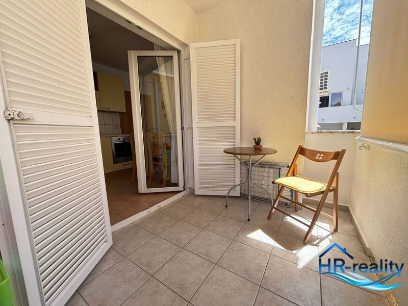 Balkon in einer 2-Zimmer-Wohnung mit weißen Jalousien und einem Holzstuhl.