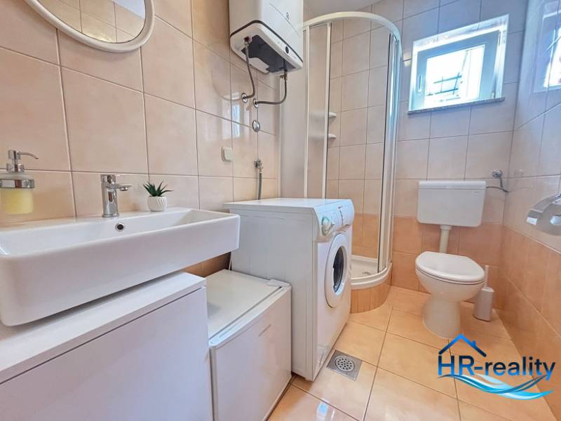 Badezimmer in einer 2-Zimmer-Wohnung mit Waschmaschine, Duschkabine und Toilette.