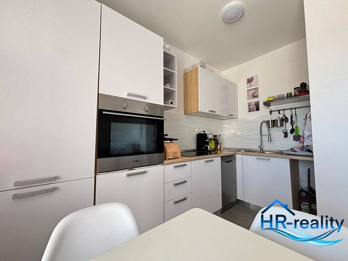 Küche in einer 2-Zimmer-Wohnung mit modernen weißen Schränken und eingebauten Geräten.