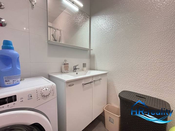 Badezimmer in einer 2-Zimmer-Wohnung mit Waschmaschine, Waschbecken und Stauraum.