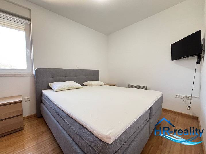 Schlafzimmer mit Doppelbett, Fernseher und Nachttischen in einer Zweizimmerwohnung.