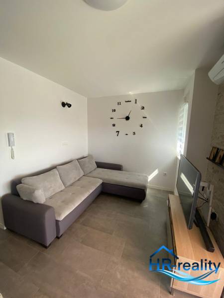 Wohnzimmer in einer 2-Zimmer-Wohnung mit Sofa, Fernseher und Wanduhr.