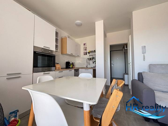 Küche in einer 2-Zimmer-Wohnung mit weißen Geräten und einem Holzesstisch.