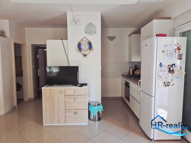 Küche in einer 2-Zimmer-Wohnung mit Geräten, Schrank, Fernseher und Wanddekoration.
