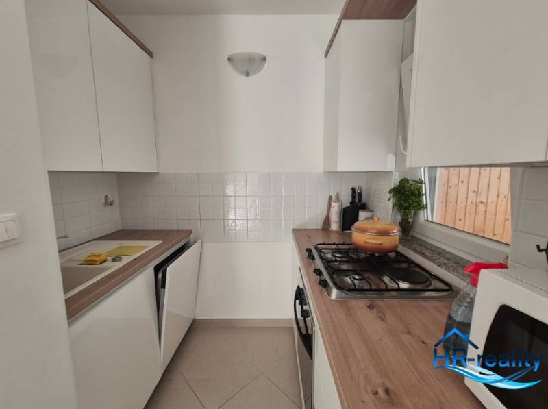 Küche in einer 2-Zimmer-Wohnung, helle Schränke, Herd, Mikrowelle, Holzarbeitsplatte.
