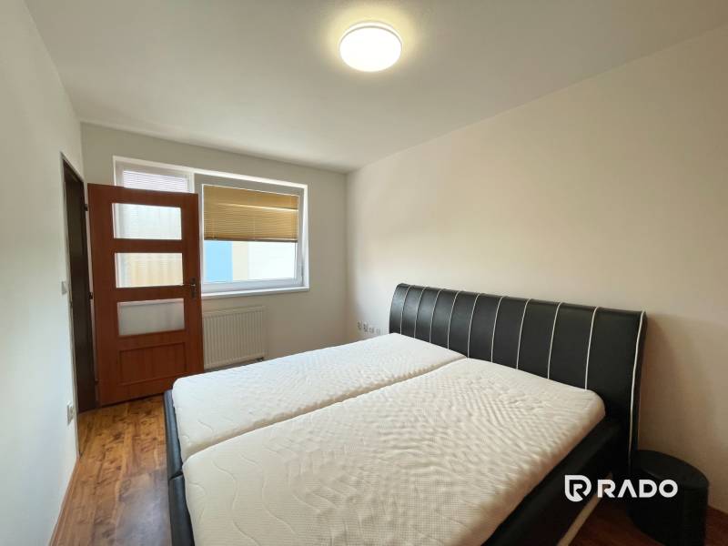 Schlafzimmer mit Doppelbett, Tür und großem Fenster in einer 2-Zimmer-Wohnung.