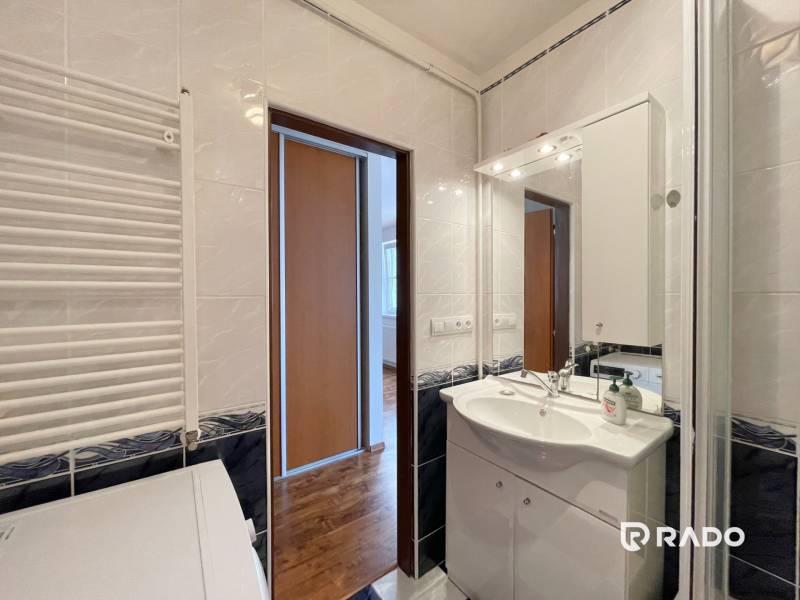 Badezimmer in einer 2-Zimmer-Wohnung mit Spiegel und Waschbecken, sichtbarer Flur und Korridor.