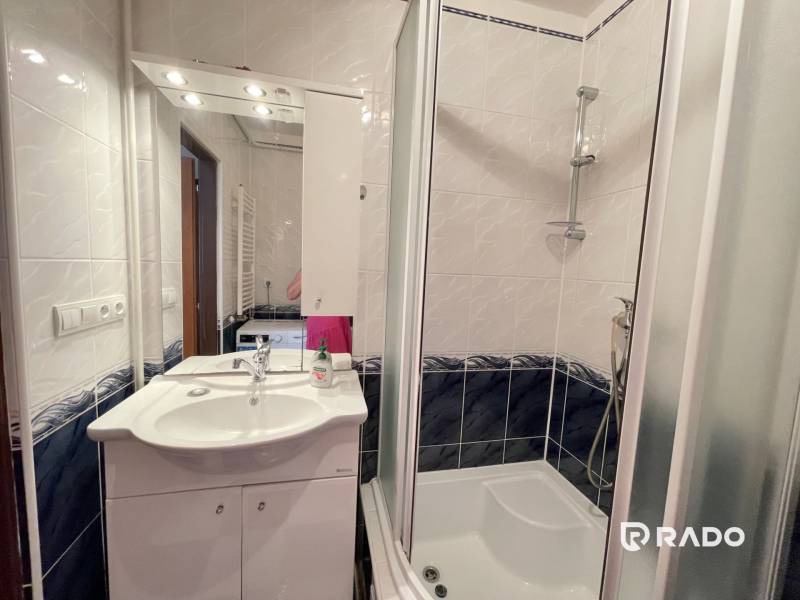 Badezimmer in einer 2-Zimmer-Wohnung mit Waschbecken, Dusche und Spiegel über dem Schrank.