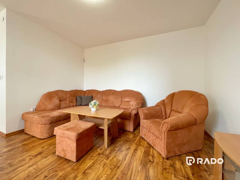 Wohnzimmer mit einer orangefarbenen Couch in einer Zweizimmerwohnung mit Holzboden.