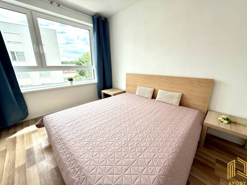 Helles Schlafzimmer mit großem Fenster und Holzbett in einer 2-Zimmer-Wohnung.