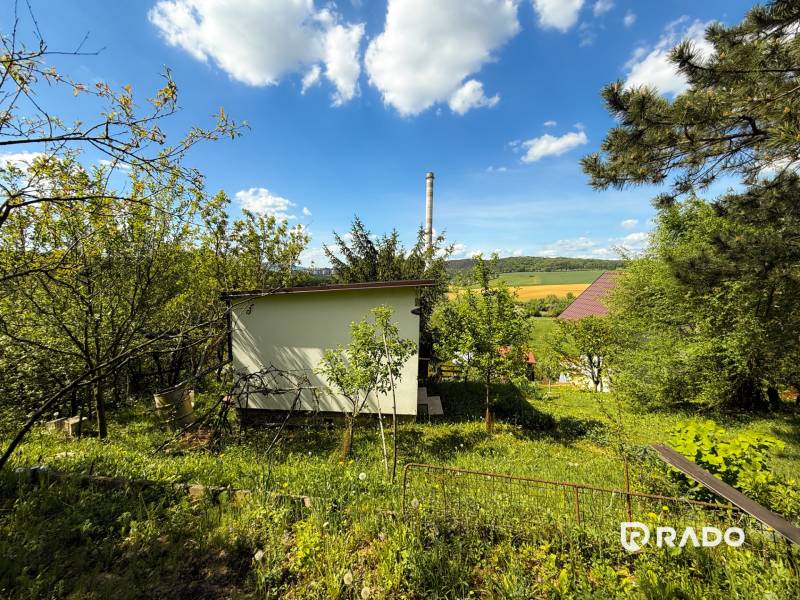 Gärten in Trenčín mit Grünflächen, einem Häuschen und Blick auf Felder und Wälder.