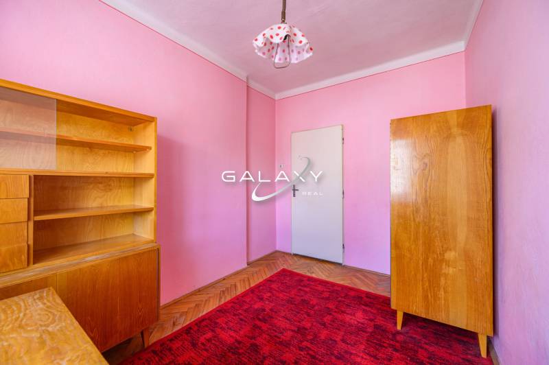 Ein Zimmer in einem Einfamilienhaus mit Holzmöbeln, rotem Teppich und rosa Wänden.