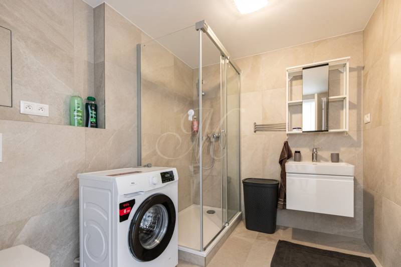 Badezimmer in einer Einzimmerwohnung mit Waschmaschine, Duschkabine und Waschbecken.