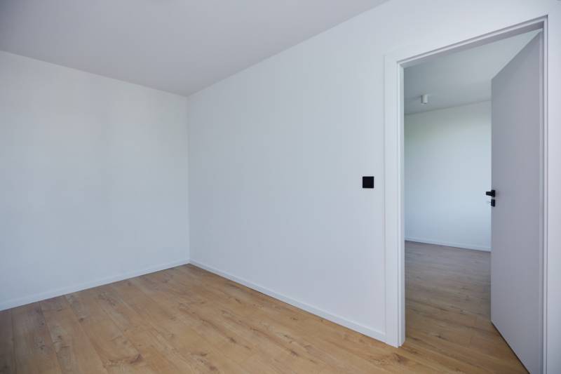 Ein leerer Raum mit Holzboden und offenen Türen in einer Zweizimmerwohnung.