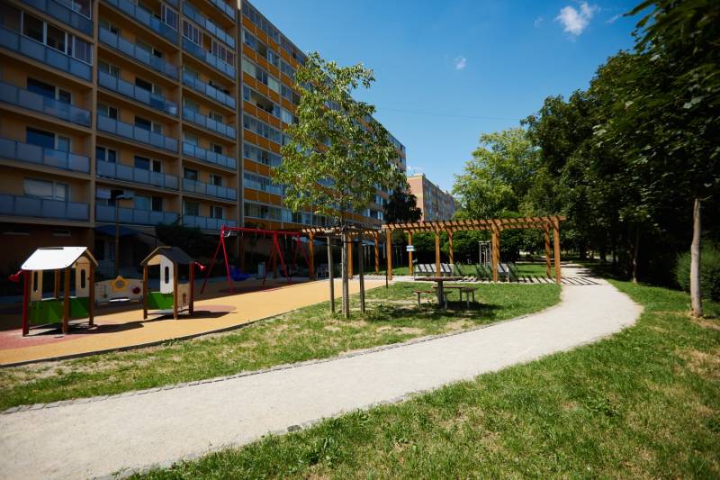 Spielplatz mit Wohngebäude im Stadtteil Juh von Košice, umgeben von Grünflächen und einem Gehweg.