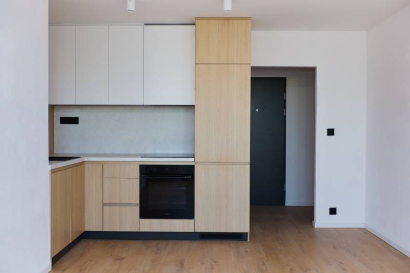 Küche in einer 2-Zimmer-Wohnung mit Holzschränken und schwarzen Geräten.