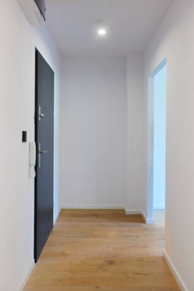 Flur mit Holzboden, weißen Wänden und Türen in einer Zweizimmerwohnung.