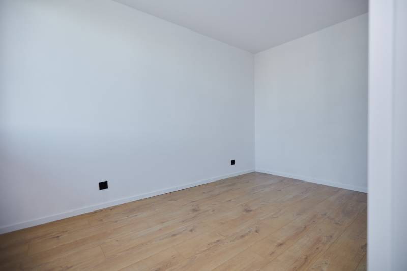 Ein leerer Raum mit weißen Wänden und Holzboden in einer Zweizimmerwohnung.