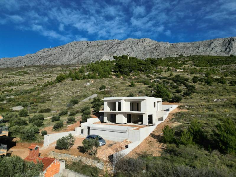 Eine Villa in Duće, umgeben von Grün und Bergen, mit blauem Himmel im Hintergrund.